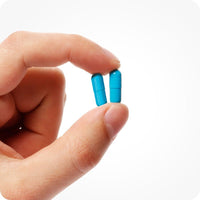 Hand holding two blue capsules of Conceive Plus Men’s Fertility Support on a white background.