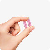 Conceive Plus Ovulation Bundle close-up of two pink fertility capsules held between fingers, demonstrating capsule size and color on a light background for visual reference.