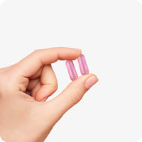Conceive Plus Ovulation Bundle close-up of two pink fertility capsules held between fingers, demonstrating capsule size and color on a light background for visual reference.