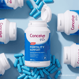 A bottle of Conceive Plus Men's Fertility Support dietary supplement lies open on a light blue background, surrounded by scattered blue capsules and additional Conceive Plus bottles.