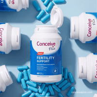 A bottle of Conceive Plus Men's Fertility Support dietary supplement lies open on a light blue background, surrounded by scattered blue capsules and additional Conceive Plus bottles.